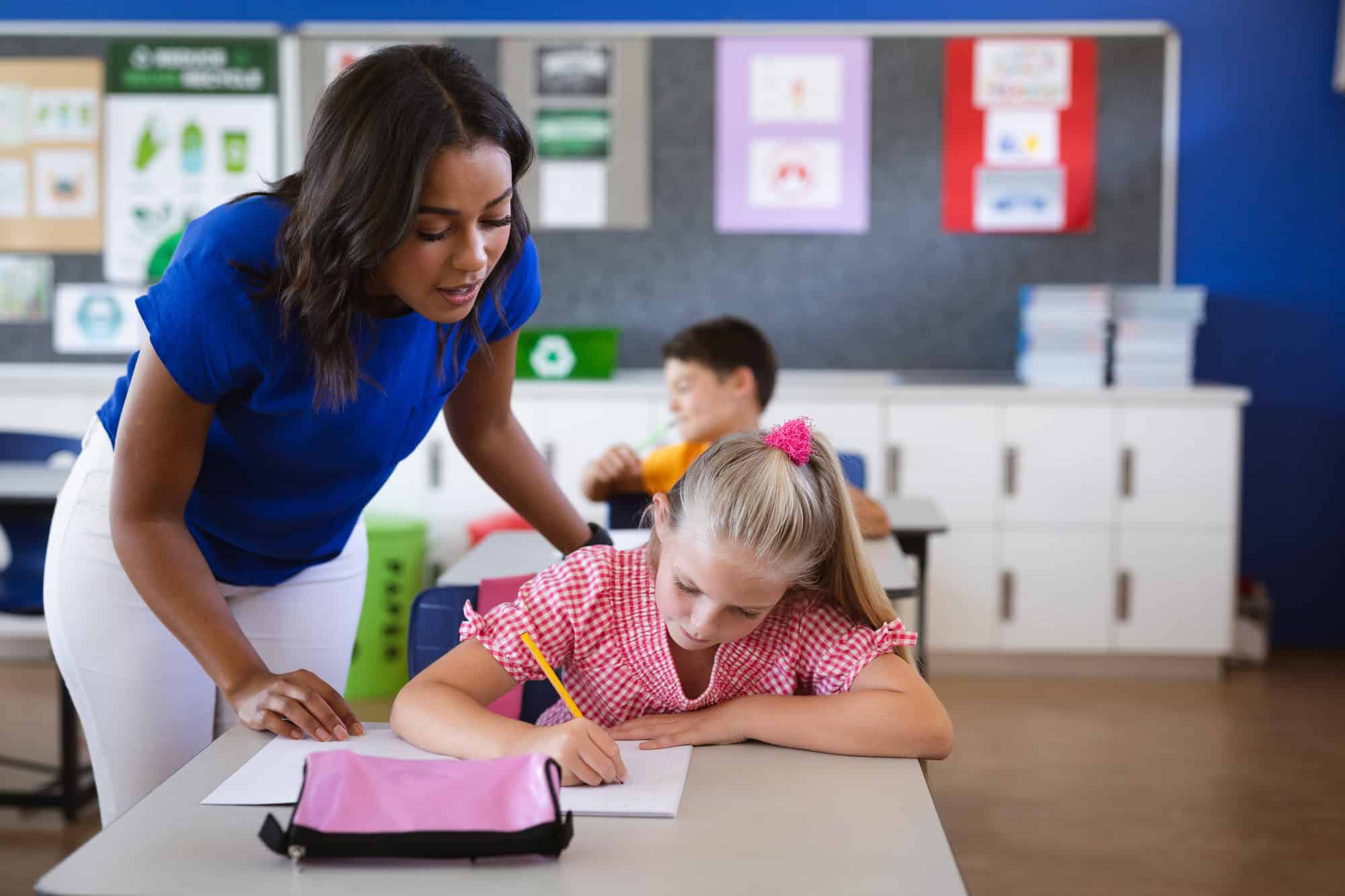 African American Female Teacher Teaching Caucasian Girl In The Class At Elementary School. School And Education Concept
